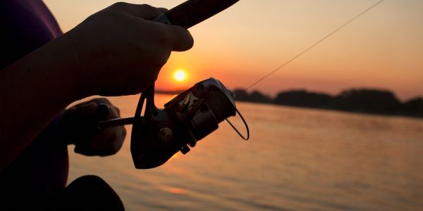 A person fishing silhouetted against a sunset on the water