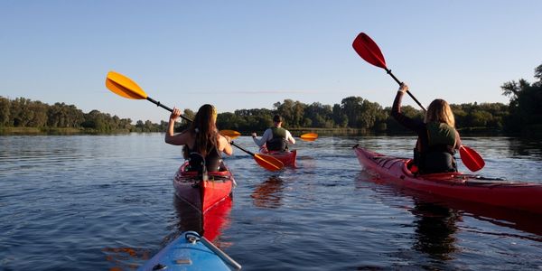 Three kayakers paddling on a river on a summer day